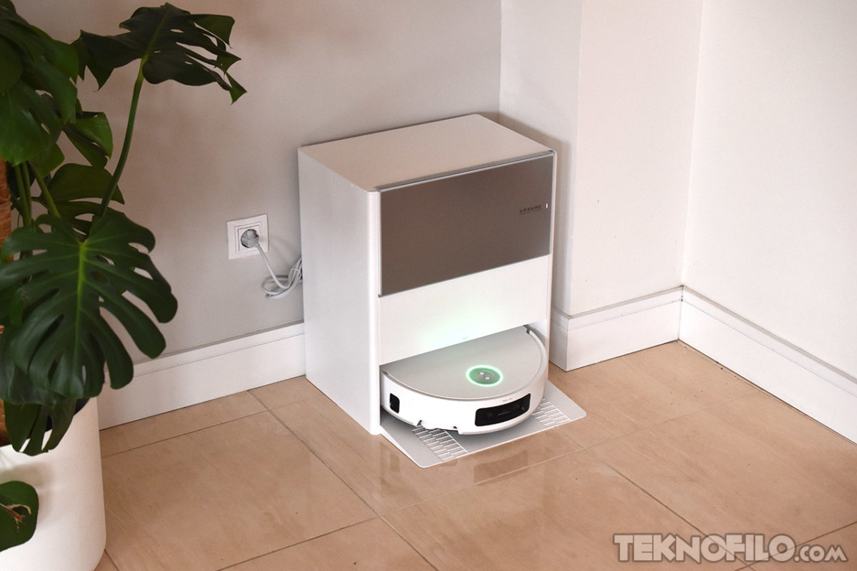 Análisis del robot aspirador Dreame Aqua10 Ultra Roller Complete Robot aspirador en estación de carga junto a planta decorativa en interior minimalista.