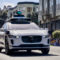 La compañía de robotaxis Waymo reconoce que a veces hay un filipino al volante Coche autónomo Jaguar blanco circulando por la ciudad bajo luz verde. Innovación en la movilidad urbana.