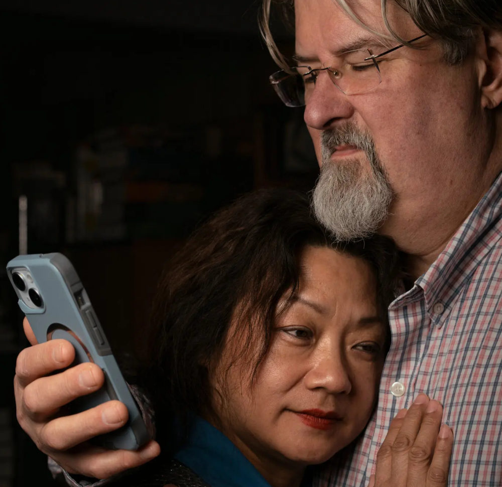 Pareja abrazada mirando un smartphone, mostrando preocupación y cercanía en un ambiente hogareño.