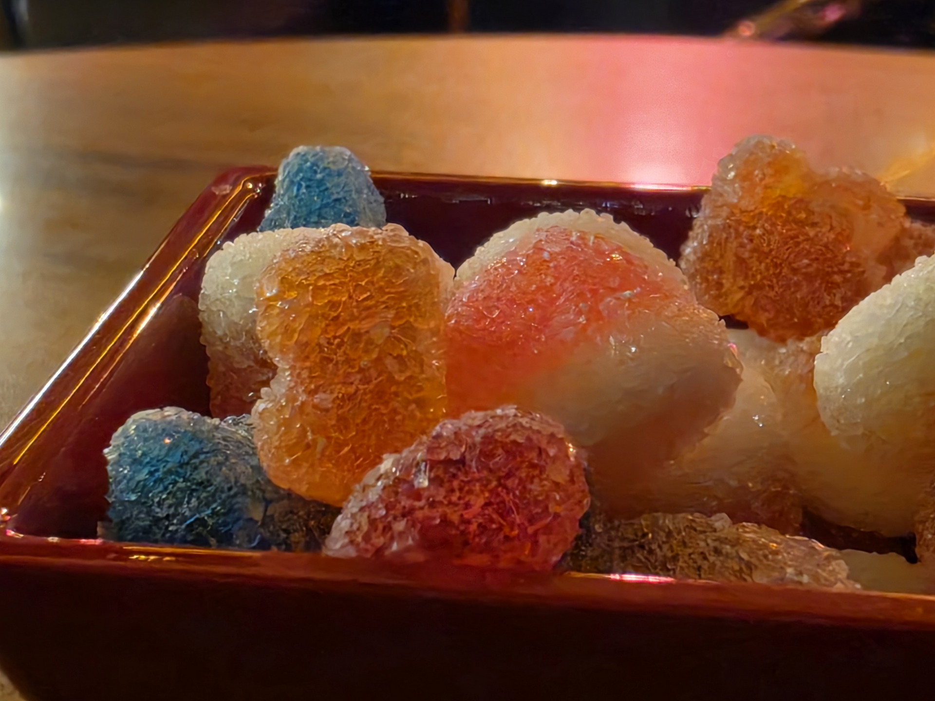 Dulces de gelatina de colores en un tazón rojo sobre la mesa, resaltando sus texturas cristalizadas.