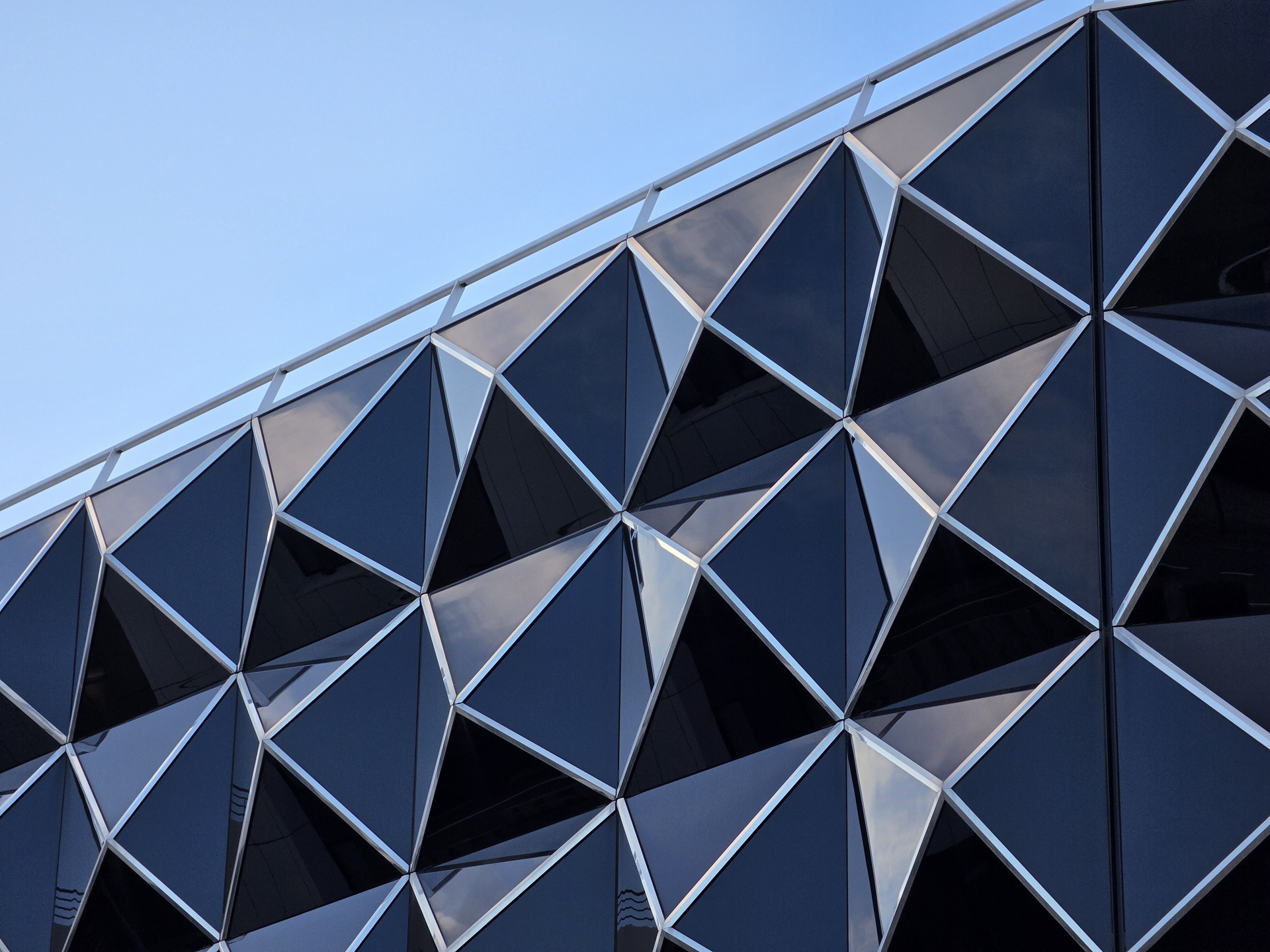 Fachada de edificio moderno con paneles de vidrio en forma de patrón geométrico triangular bajo un cielo azul.