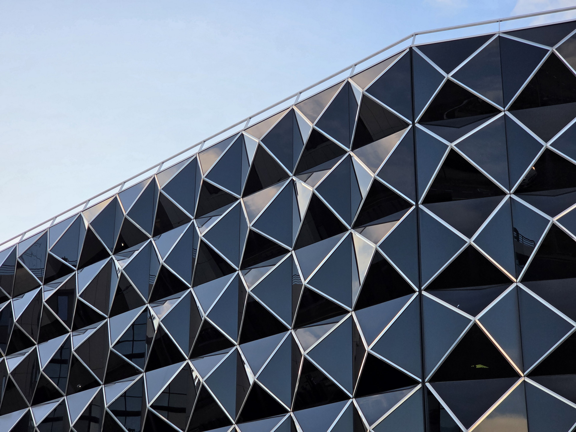 Fachada moderna de edificio con diseño geométrico de triángulos de vidrio y acero al atardecer.