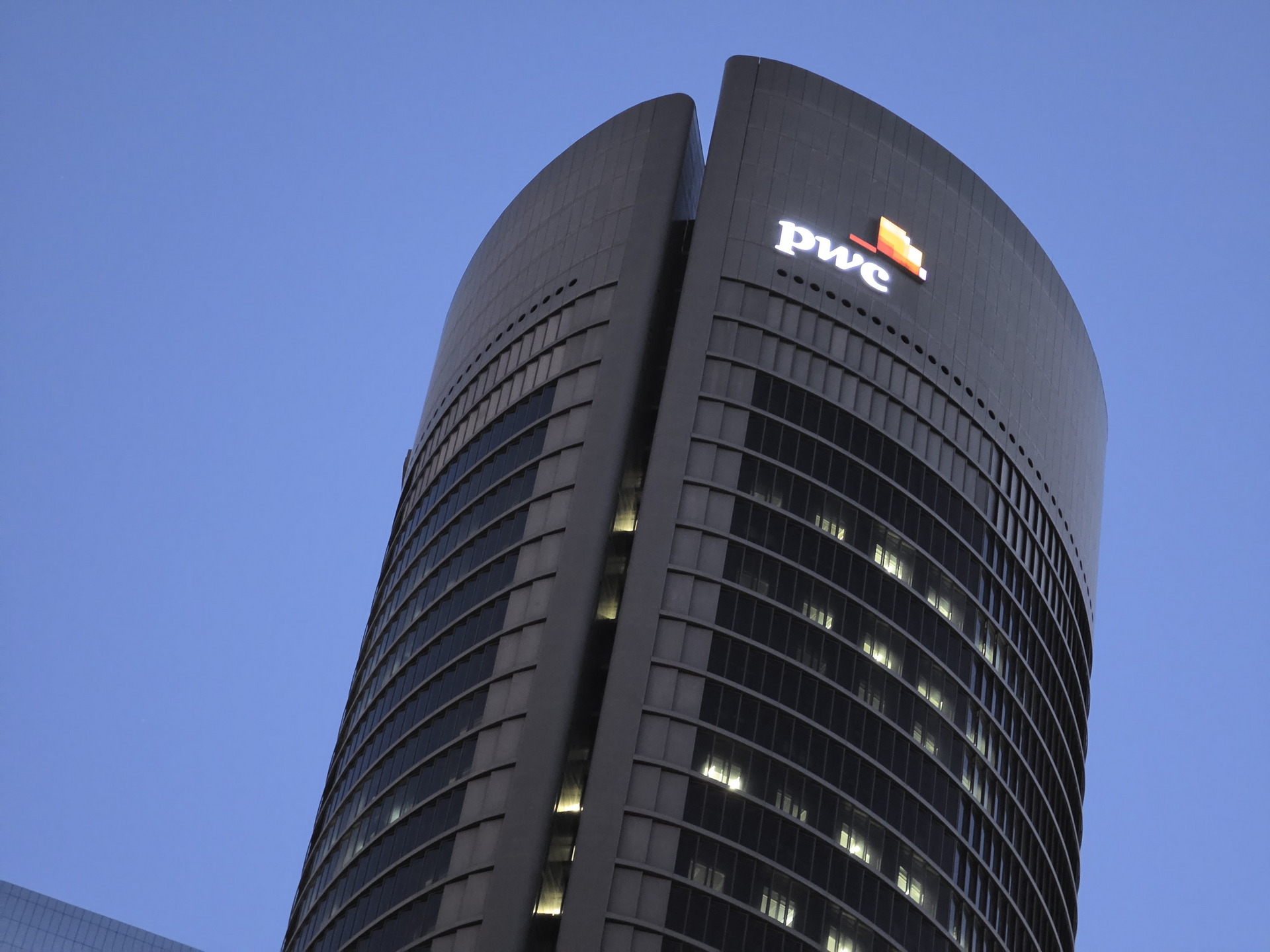 Edificio de oficinas moderno al anochecer con logo de empresa en lo alto, cielo azul de fondo.