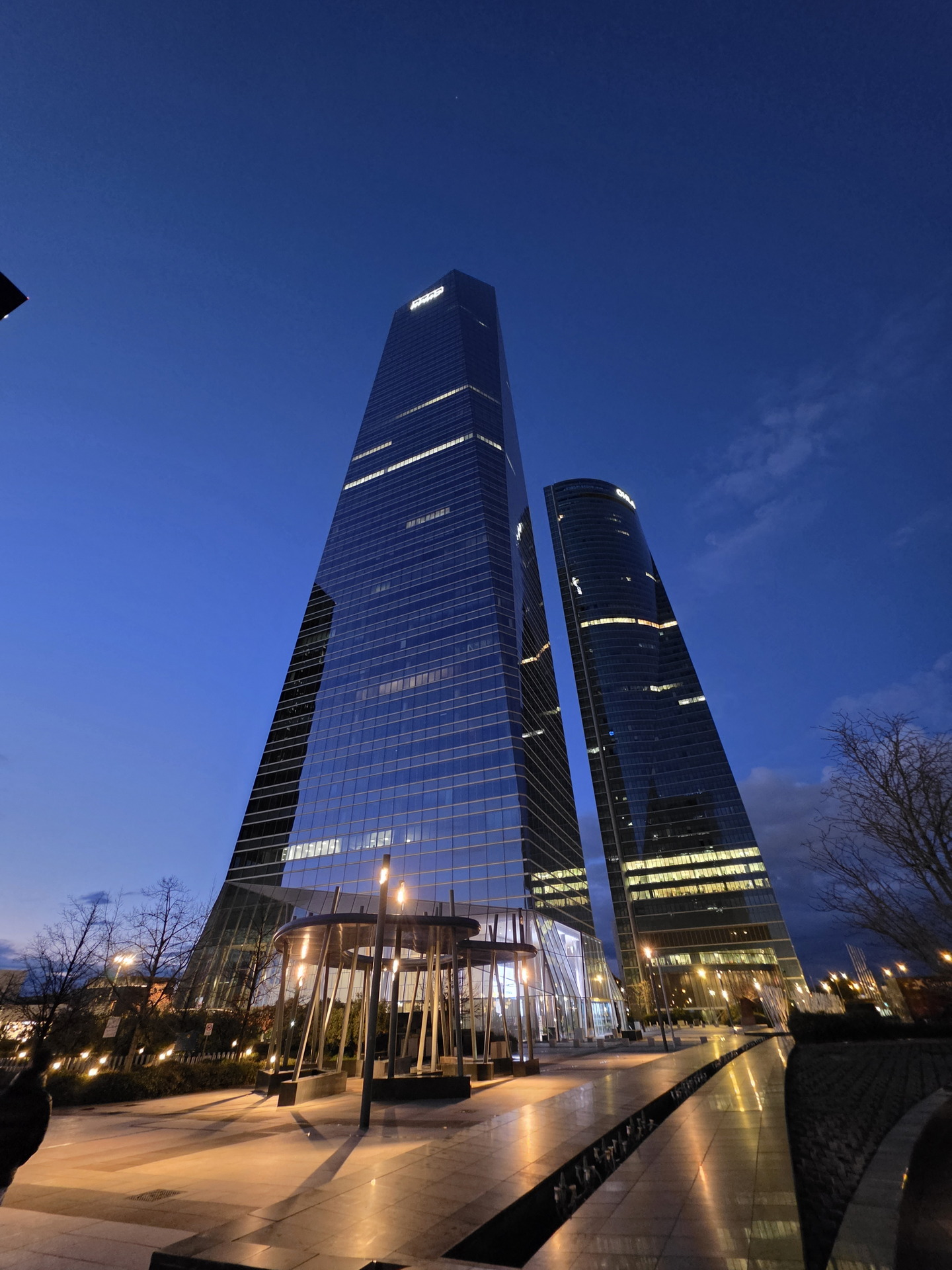 Rascacielos modernos iluminados al anochecer en una ciudad, reflejando luz en su fachada de vidrio.