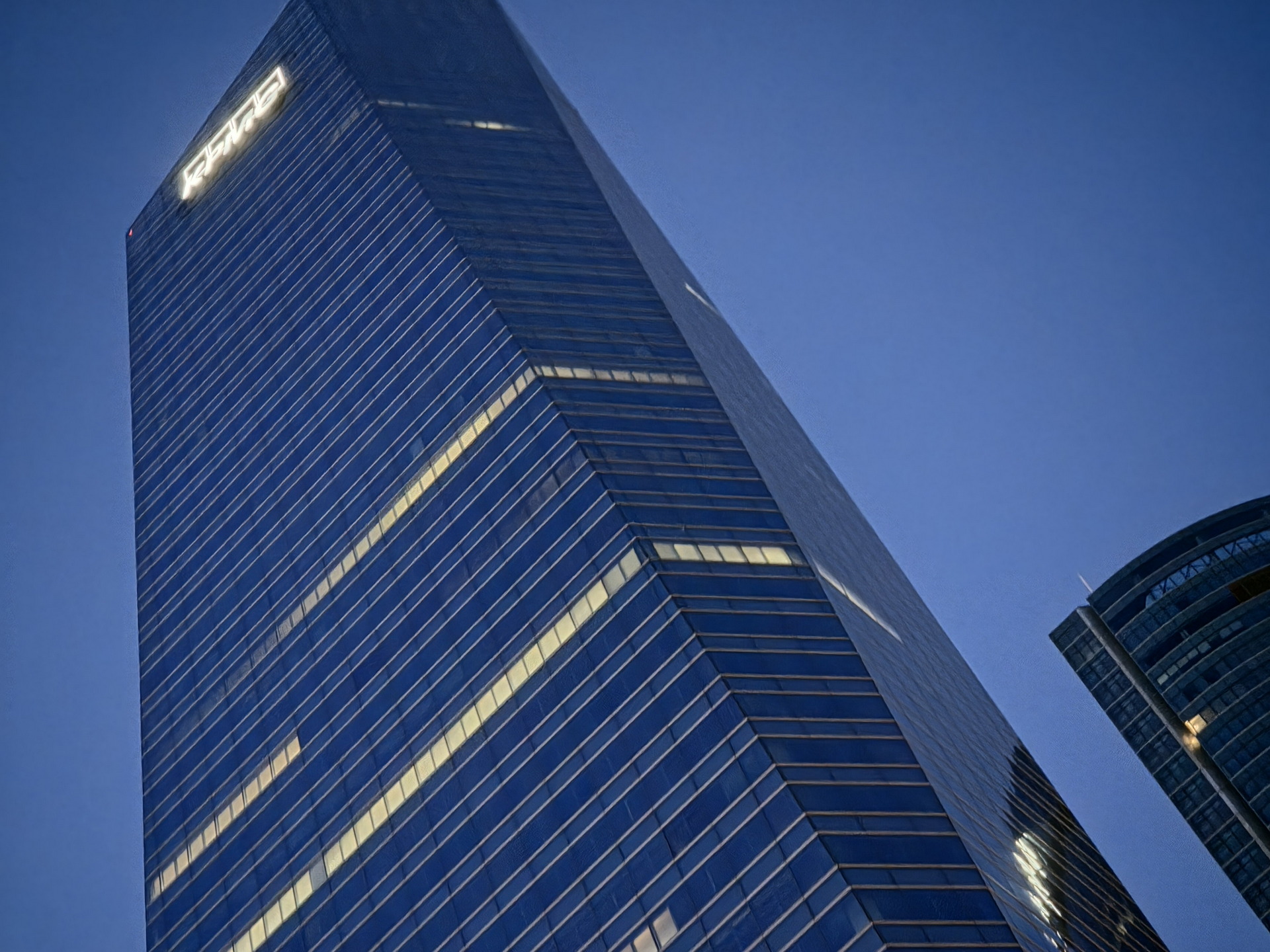 Rascacielos iluminado al anochecer en ciudad moderna, cielo azul y arquitectura de vidrio.