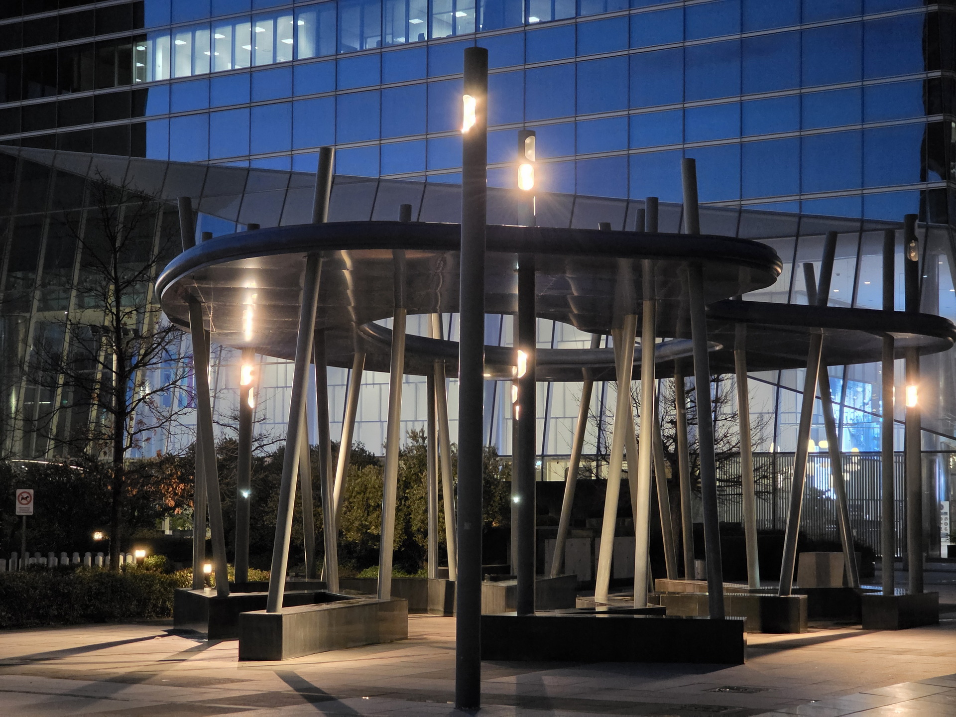 Estructura moderna iluminada frente a un edificio de cristal en la noche urbana.