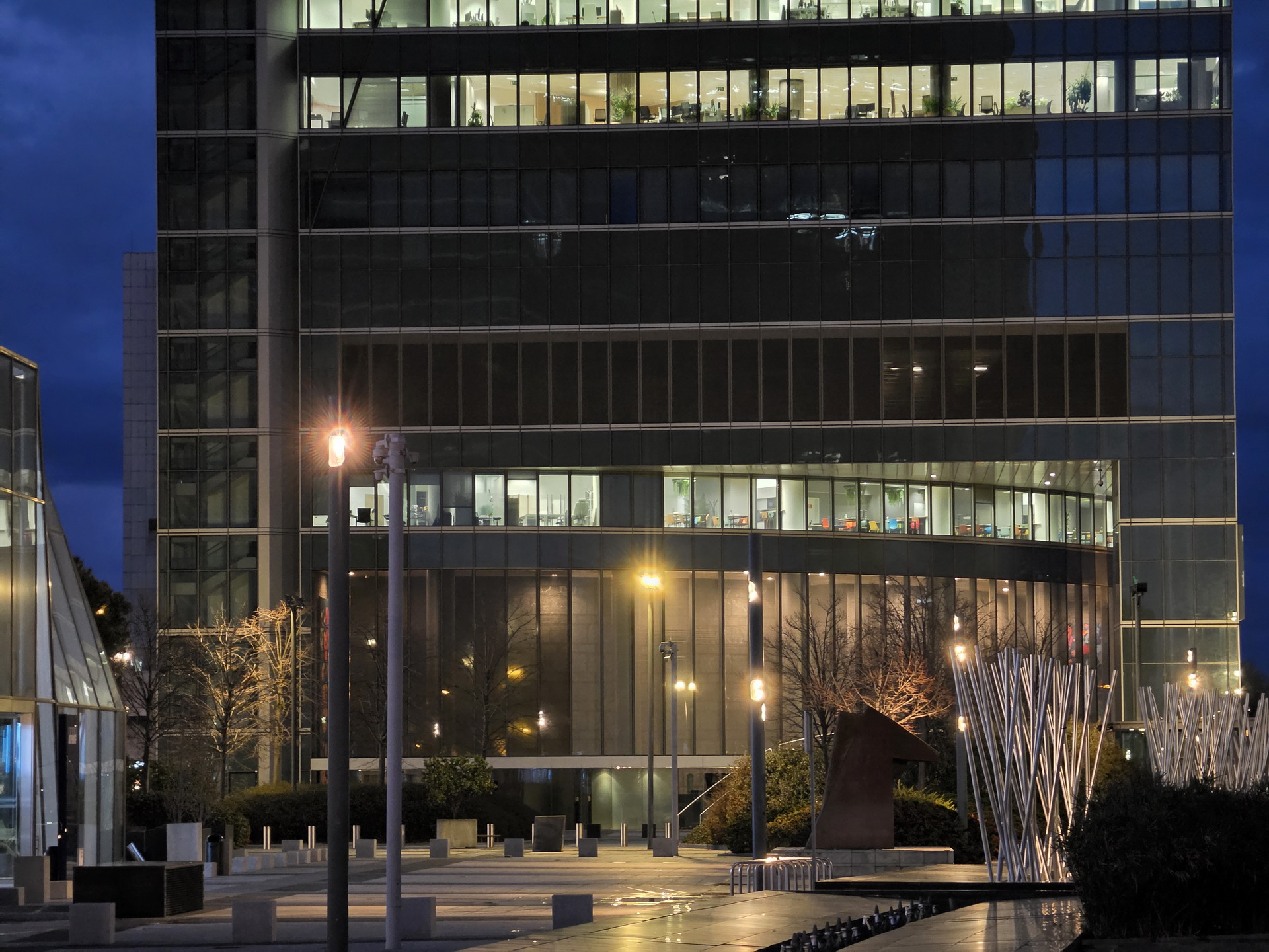 Edificio de oficinas iluminado por la noche con ventanas de vidrio y luces en la entrada.