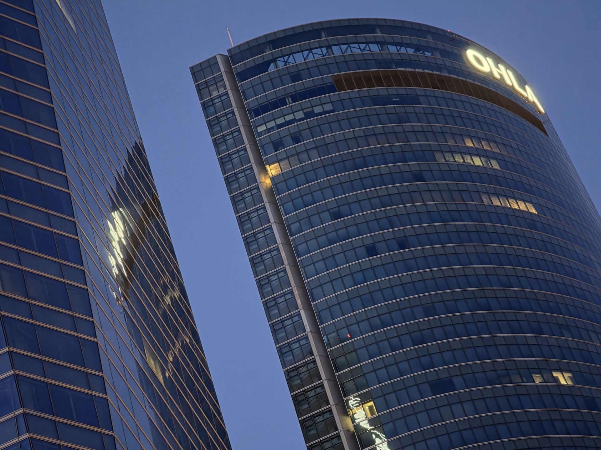 Edificios de cristal en una ciudad al atardecer, con luces reflejadas en la fachada.
