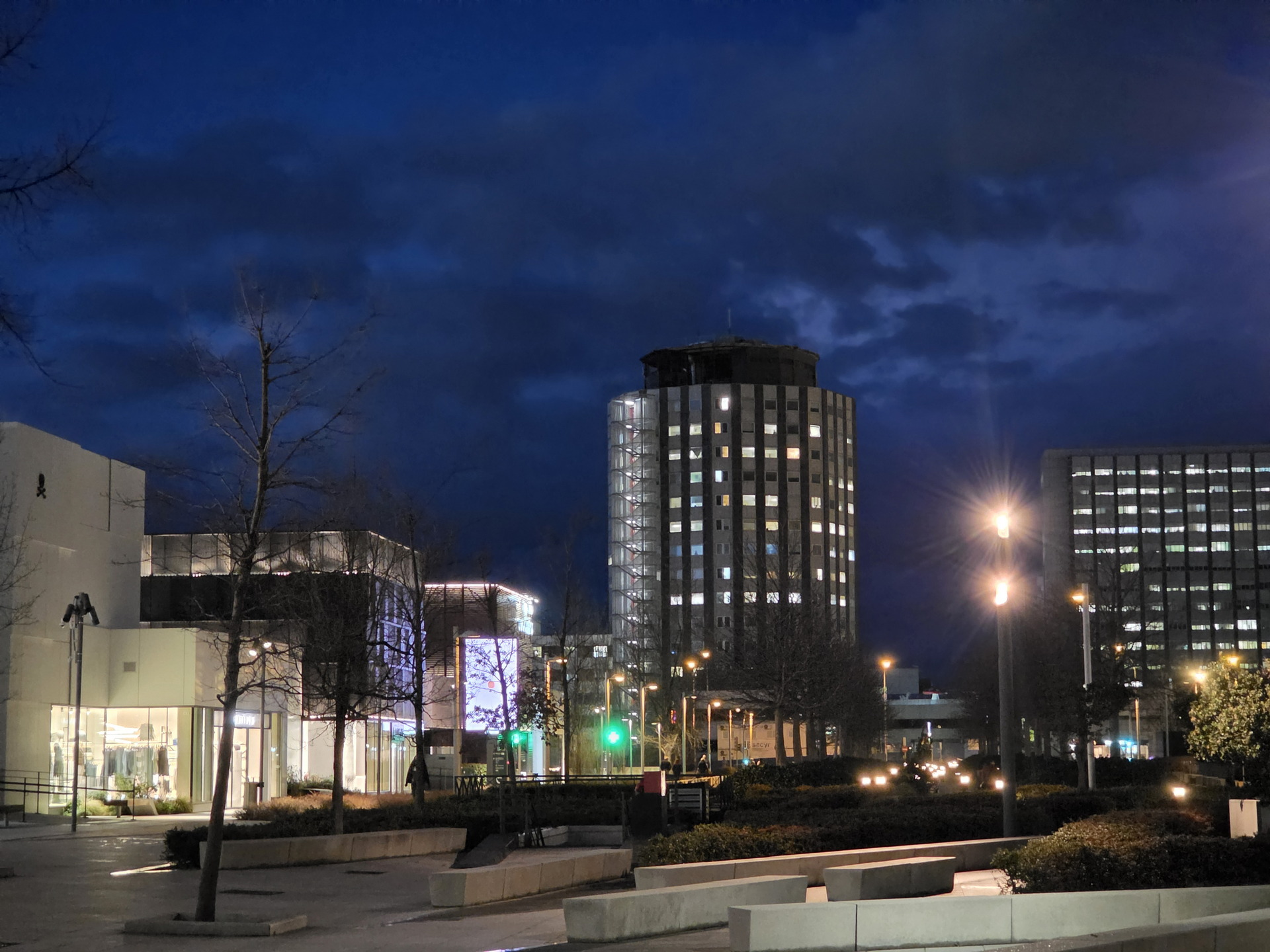 Ciudad iluminada al anochecer con edificios modernos y cielo azul oscuro.