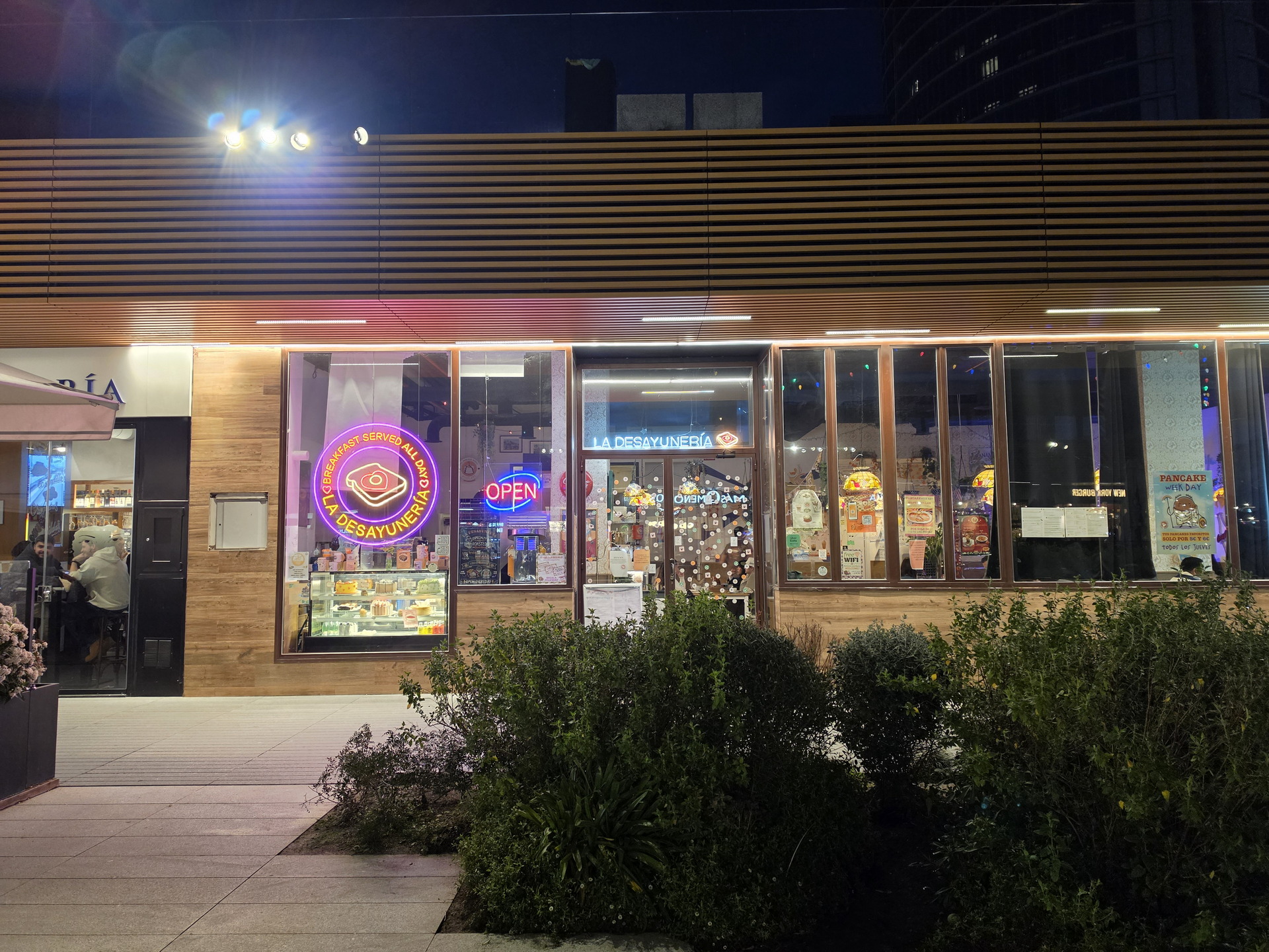 Franquicia de restaurante iluminado al anochecer, con carteles de desayuno y letrero de open en la ventana.