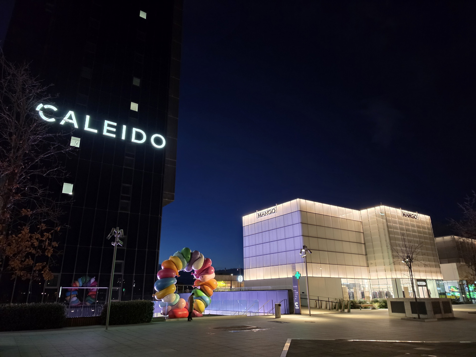 Edificio Caleido y tienda iluminados por la noche con decoración de arco colorida.