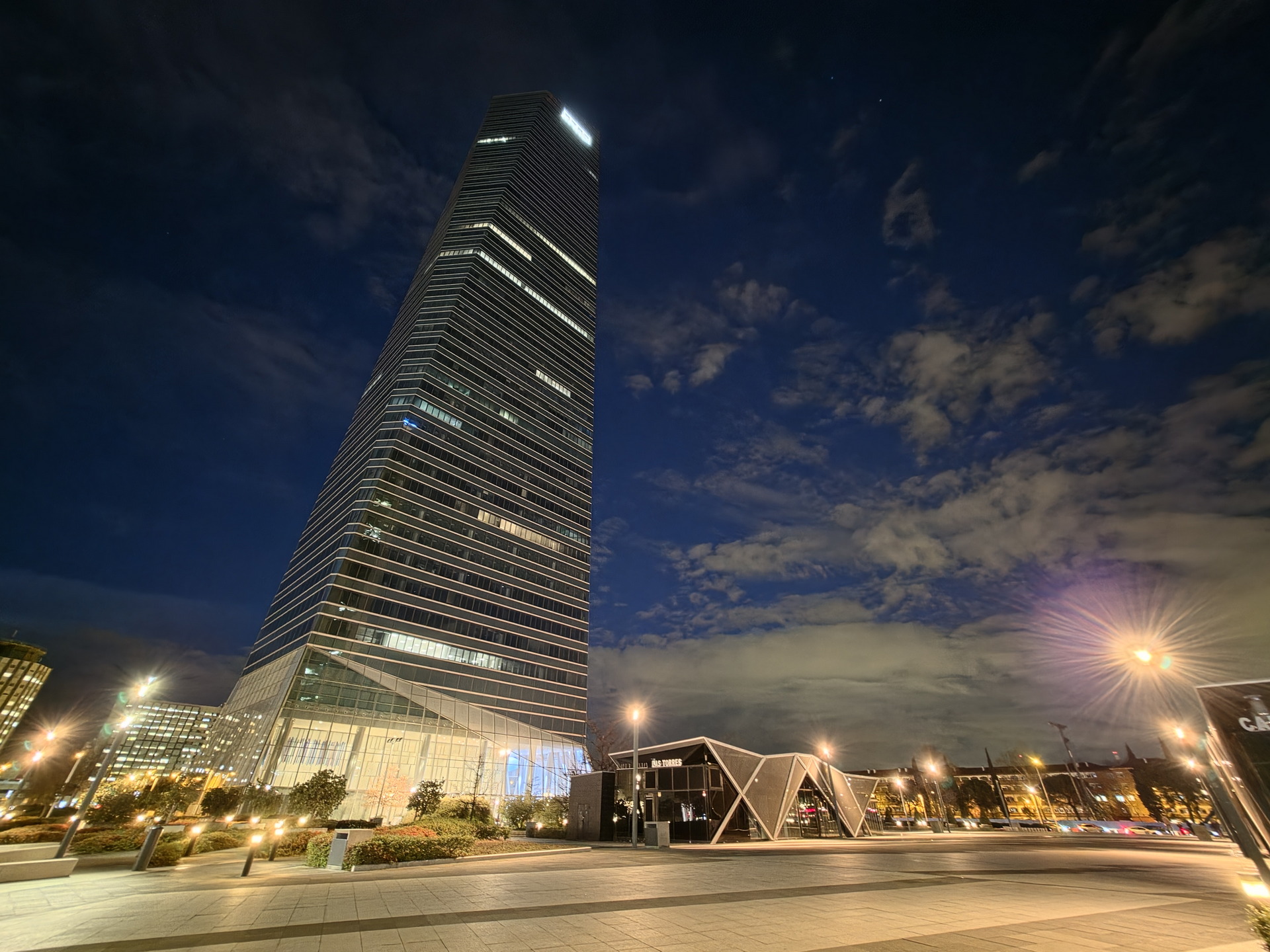 Torre iluminada de noche en el distrito financiero, cielo estrellado y luces urbanas completan la escena.