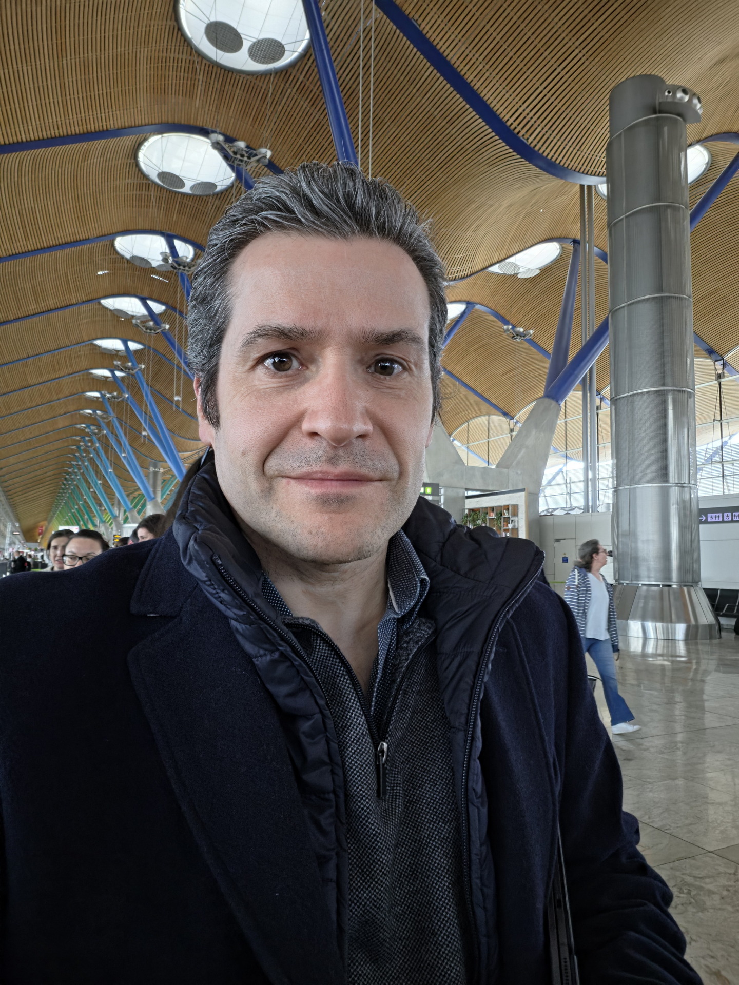 Persona en el aeropuerto con techo de madera ondulado y columnas metálicas de fondo.