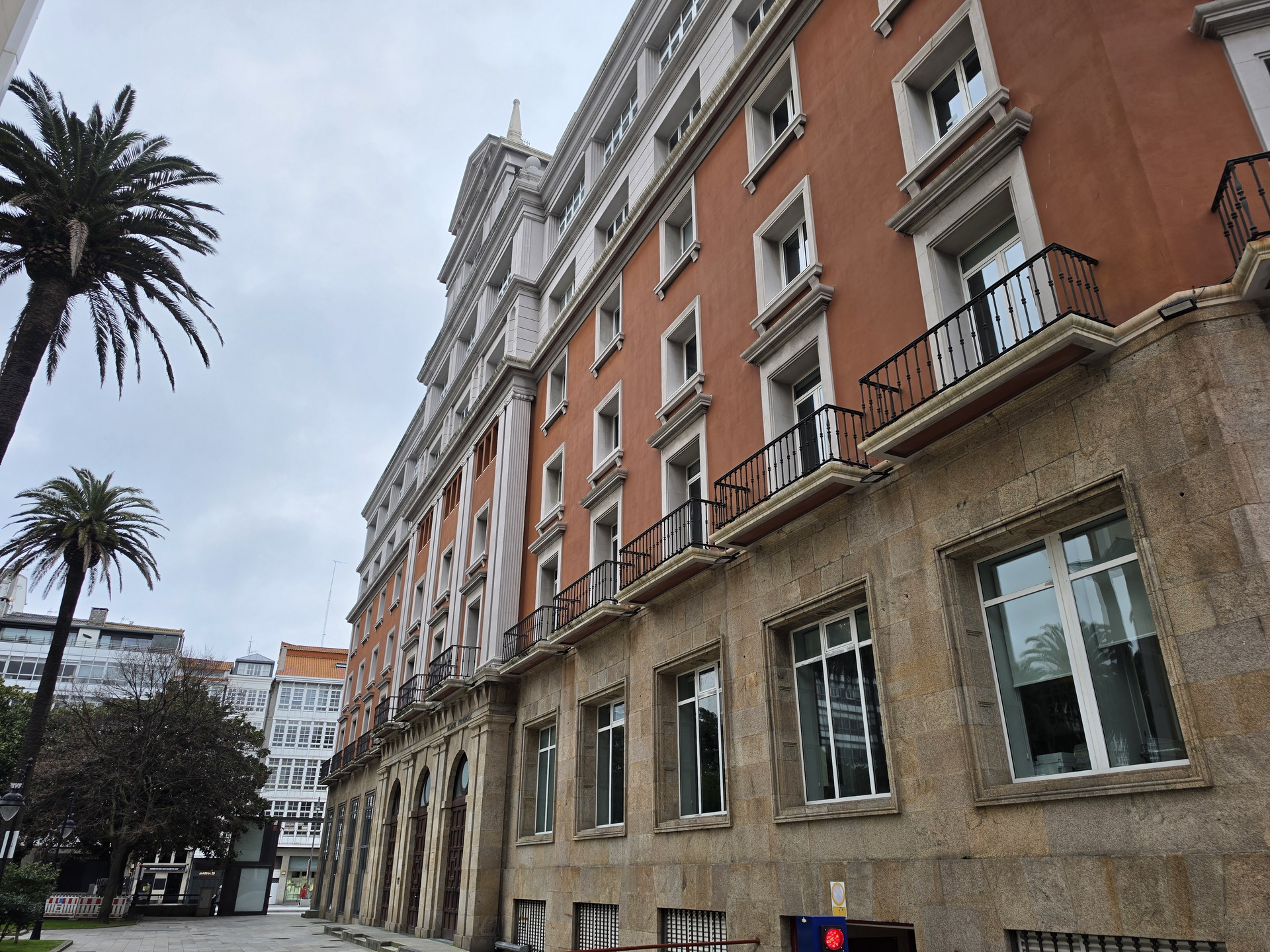 Edificio histórico color terracota con balcones; palmera y cielo nublado en la ciudad.