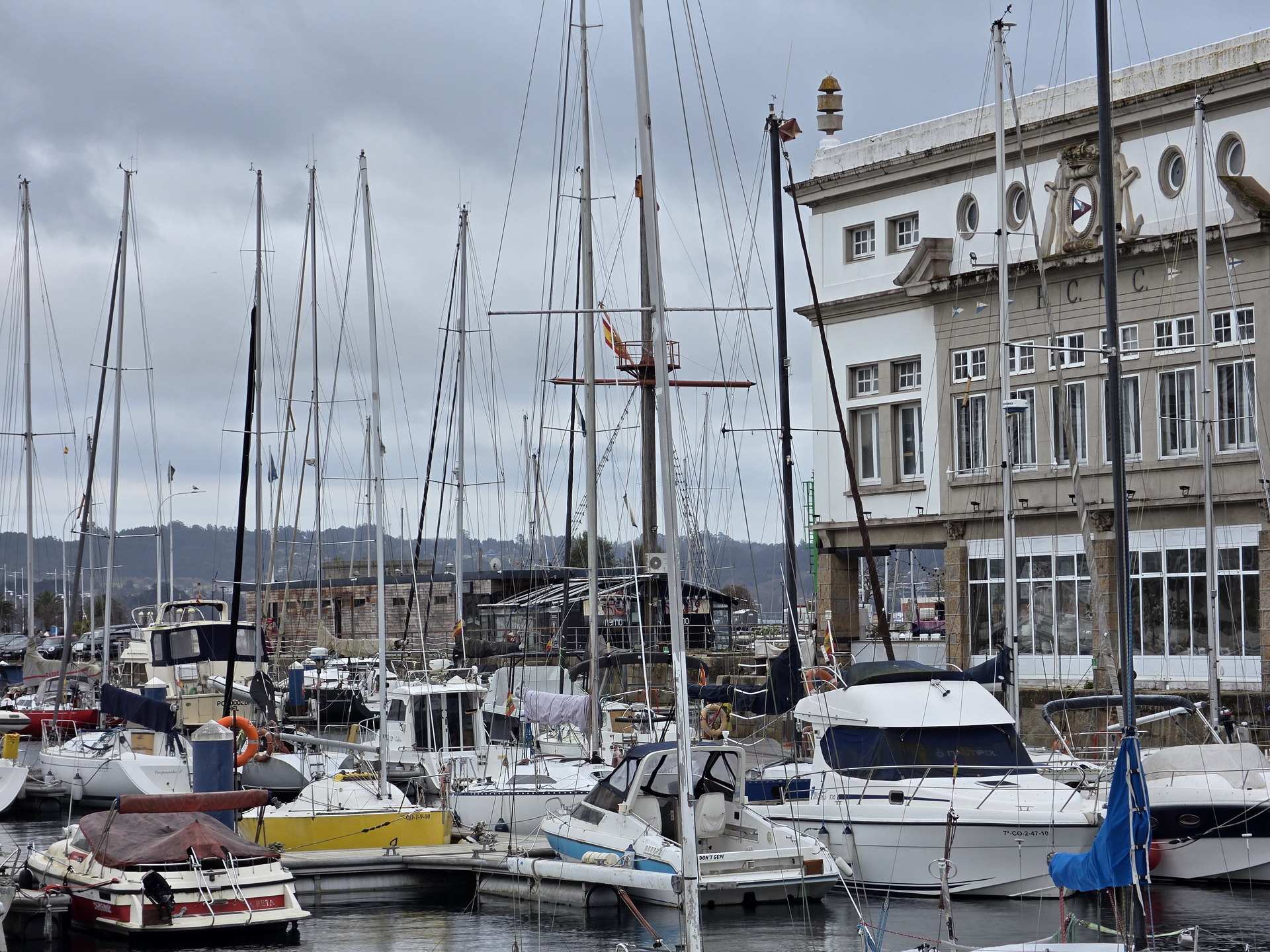 Marina con barcos y edificio histórico bajo un cielo nublado en día de invierno.