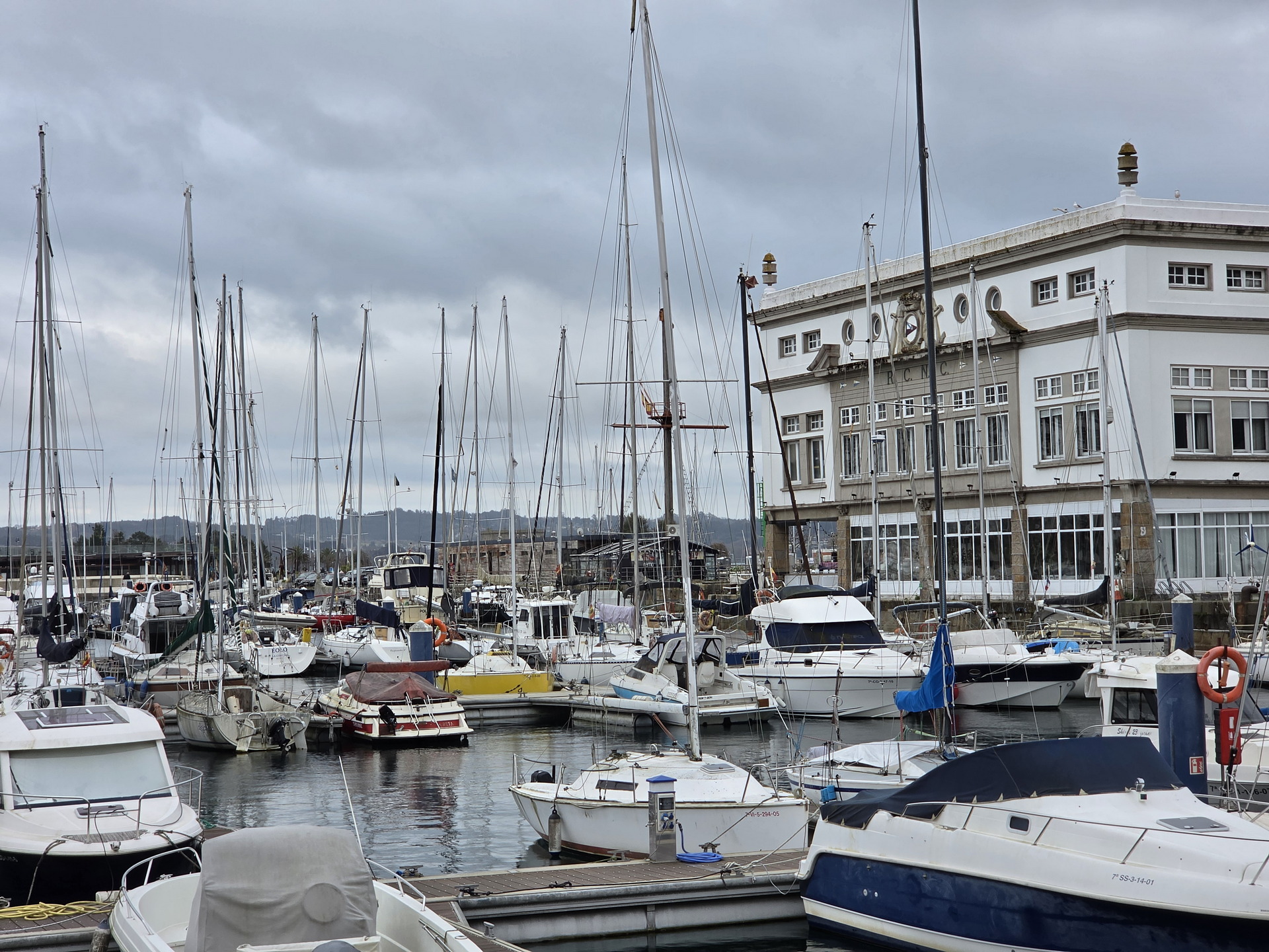 Puerto deportivo con veleros y edificio histórico en un día nublado. Ambiente náutico y marítimo.