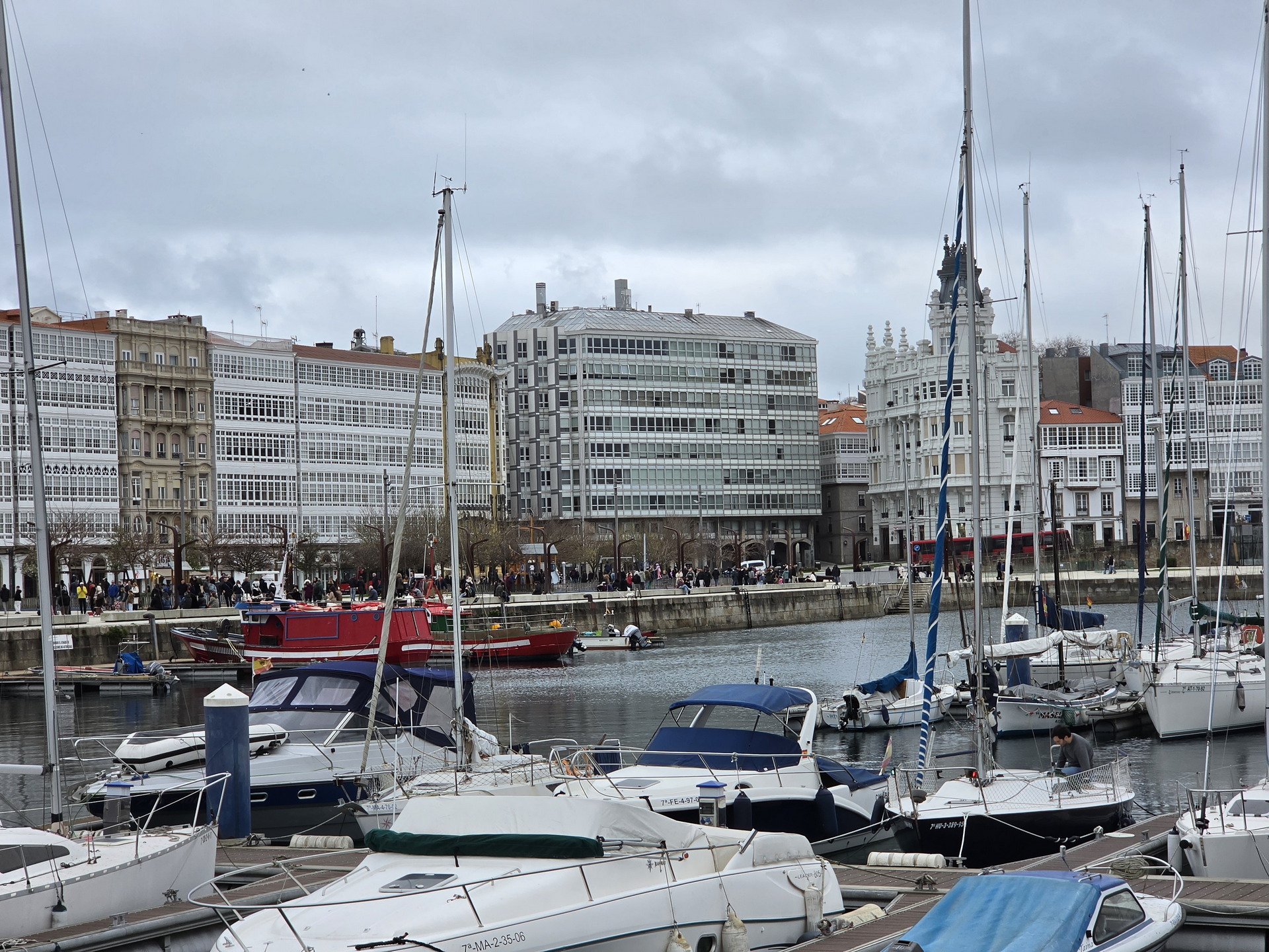 Puerto deportivo con veleros y edificios acristalados en un día nublado en A Coruña, España.