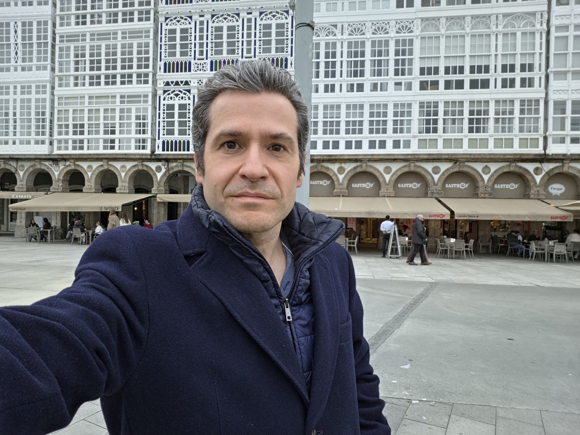 Persona en plaza frente a edificio con ventanales blancos y terrazas en A Coruña, Galicia, España.