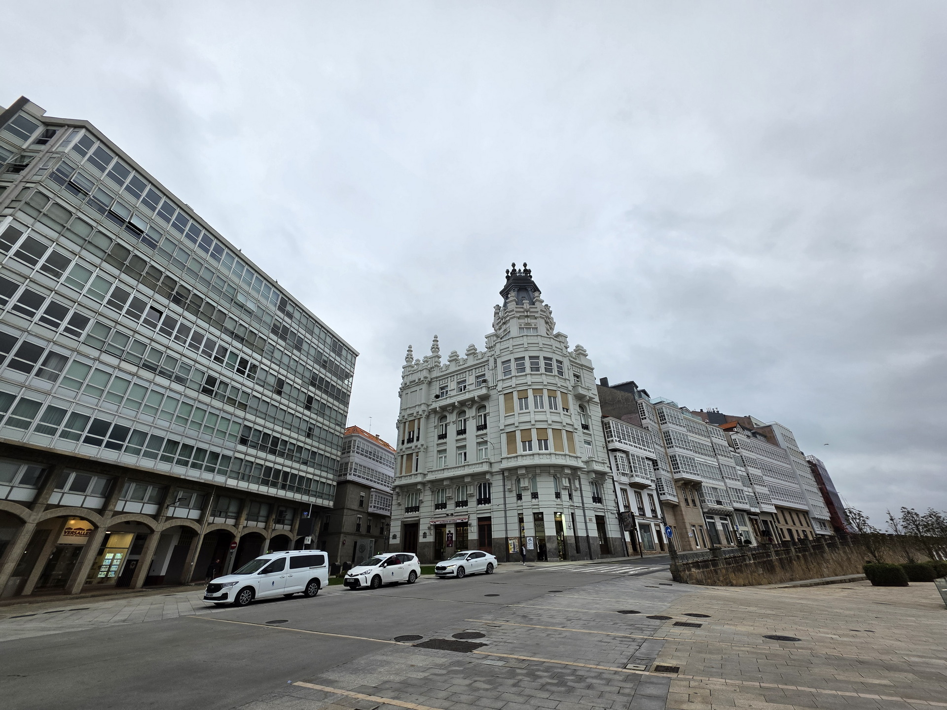 Edificios históricos con galerías acristaladas en A Coruña, cielo nublado y coches aparcados en la calle.