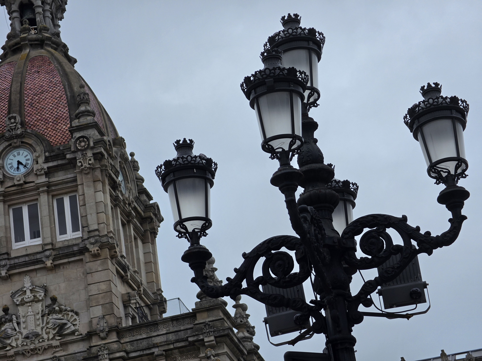 Farola ornamental y arquitectura de edificio histórico con cúpula y reloj, cielo nublado de fondo.