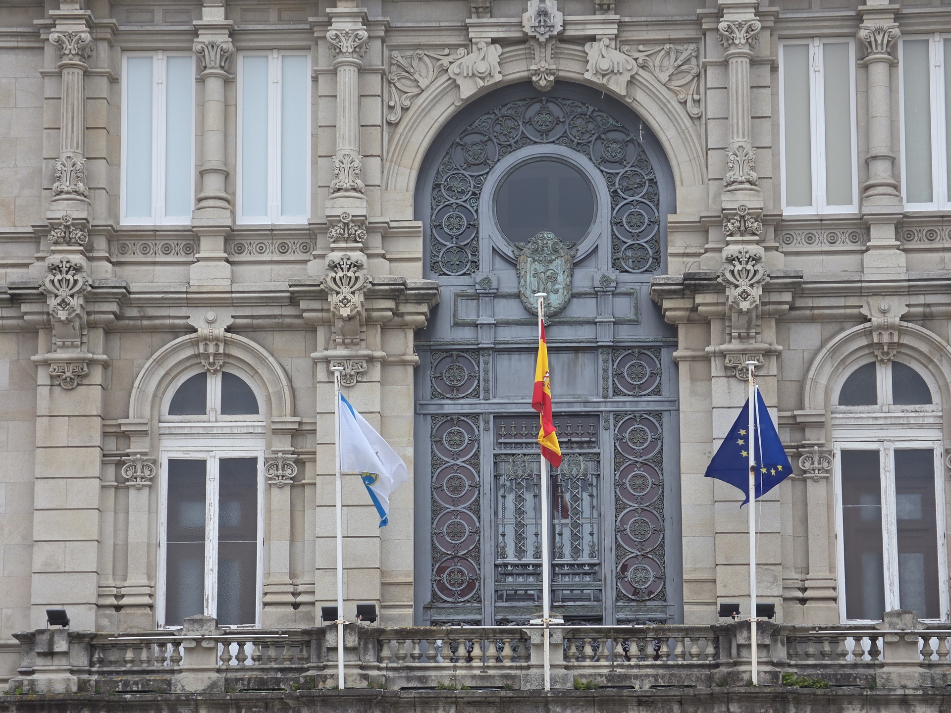 Fachada de edificio histórico con banderas de España, Galicia y la Unión Europea ondeando al frente.