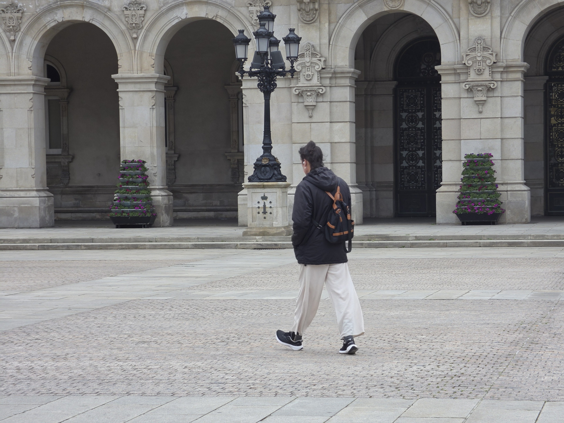 Persona caminando frente a edificio histórico con arcos y farol en un día nublado.