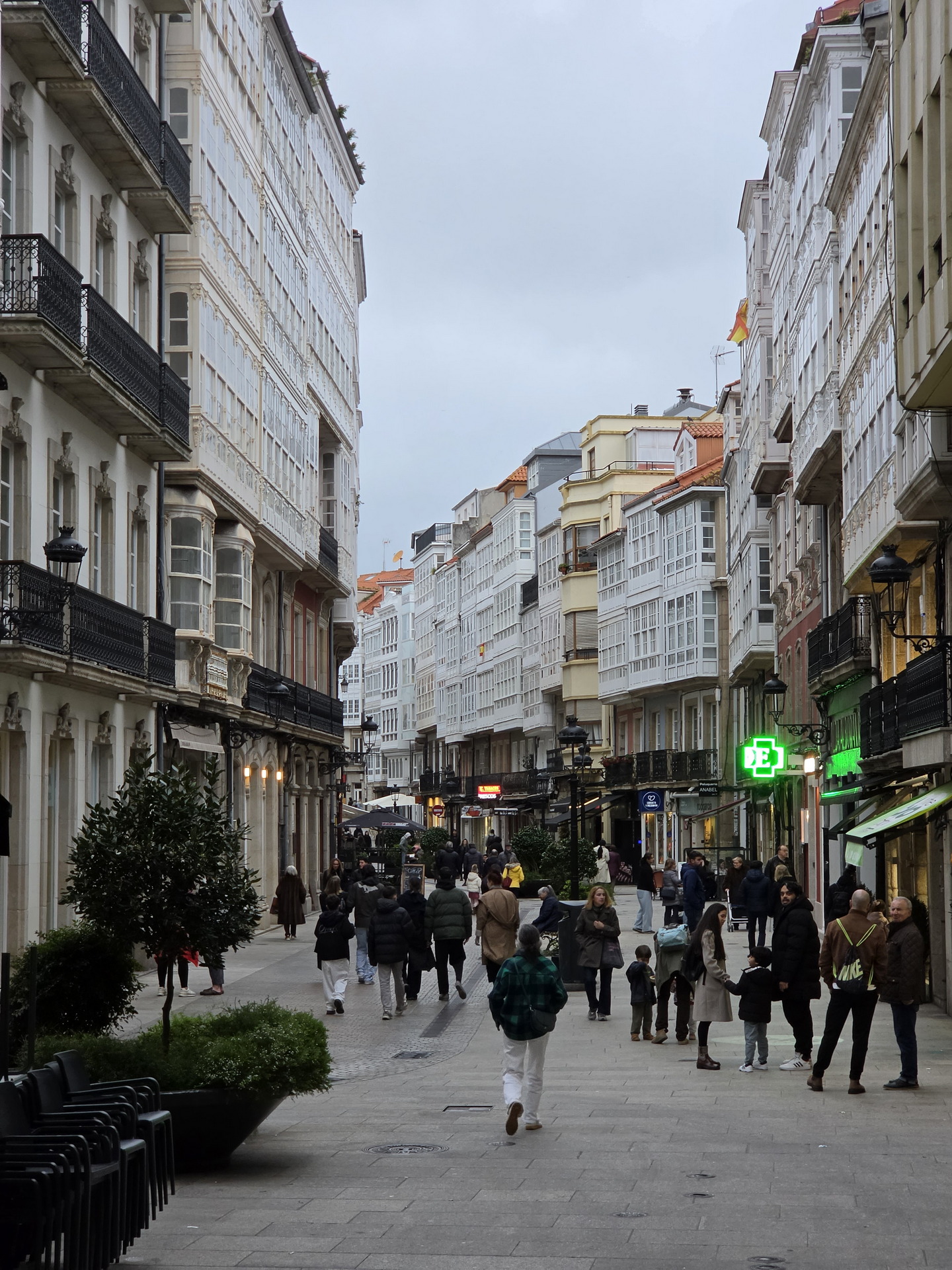 Calle peatonal en A Coruña con edificios históricos de galerías y personas caminando bajo un cielo nublado.
