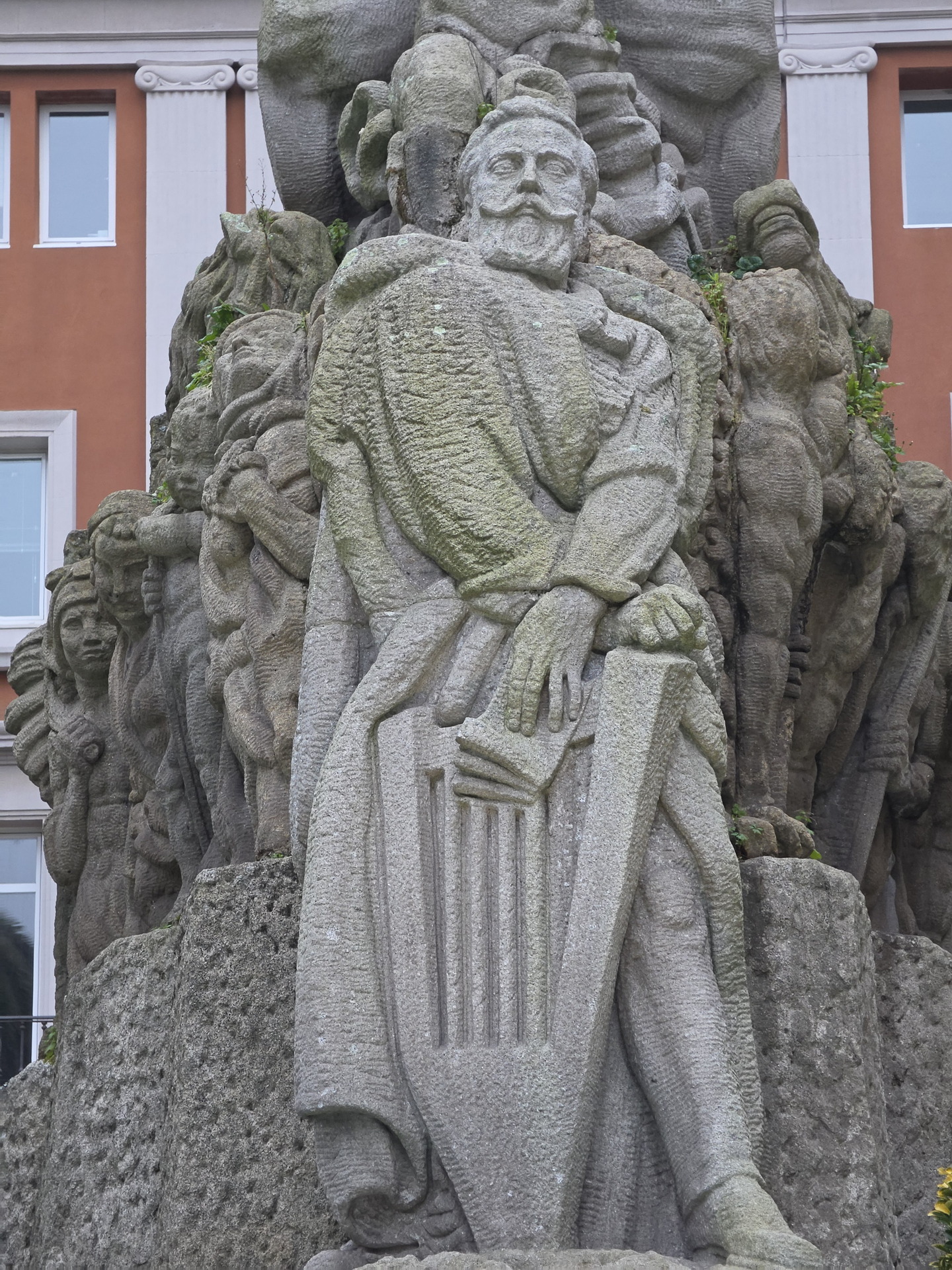 Estatua de piedra tallada en relieve, ubicada frente a edificio histórico en ciudad española.