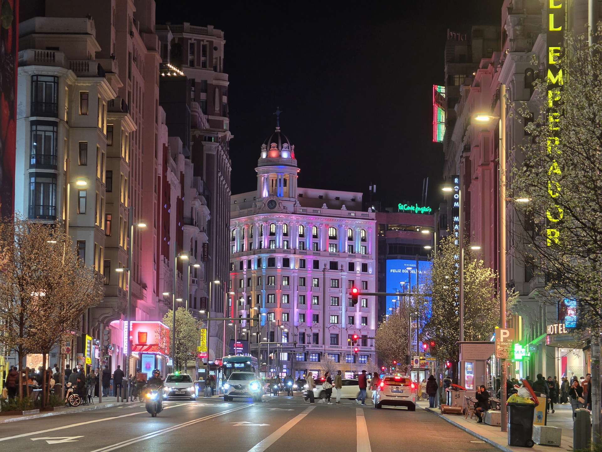 Calle Gran Vía de Madrid iluminada de noche, con edificios y luces coloridas, ambiente urbano animado.