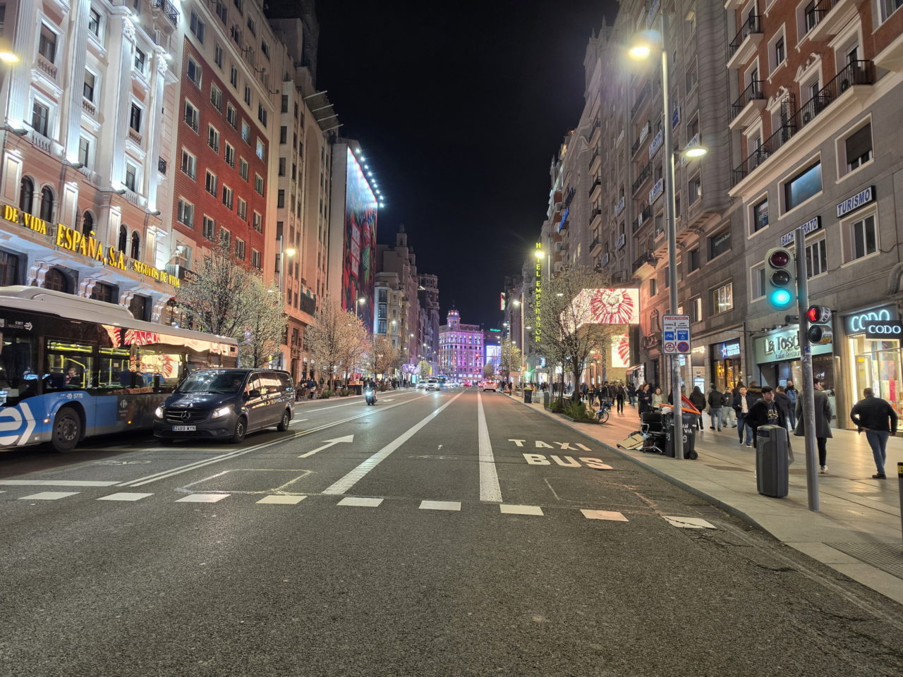 Gran Vía de Madrid iluminada por la noche con tráfico y peatones en la acera.