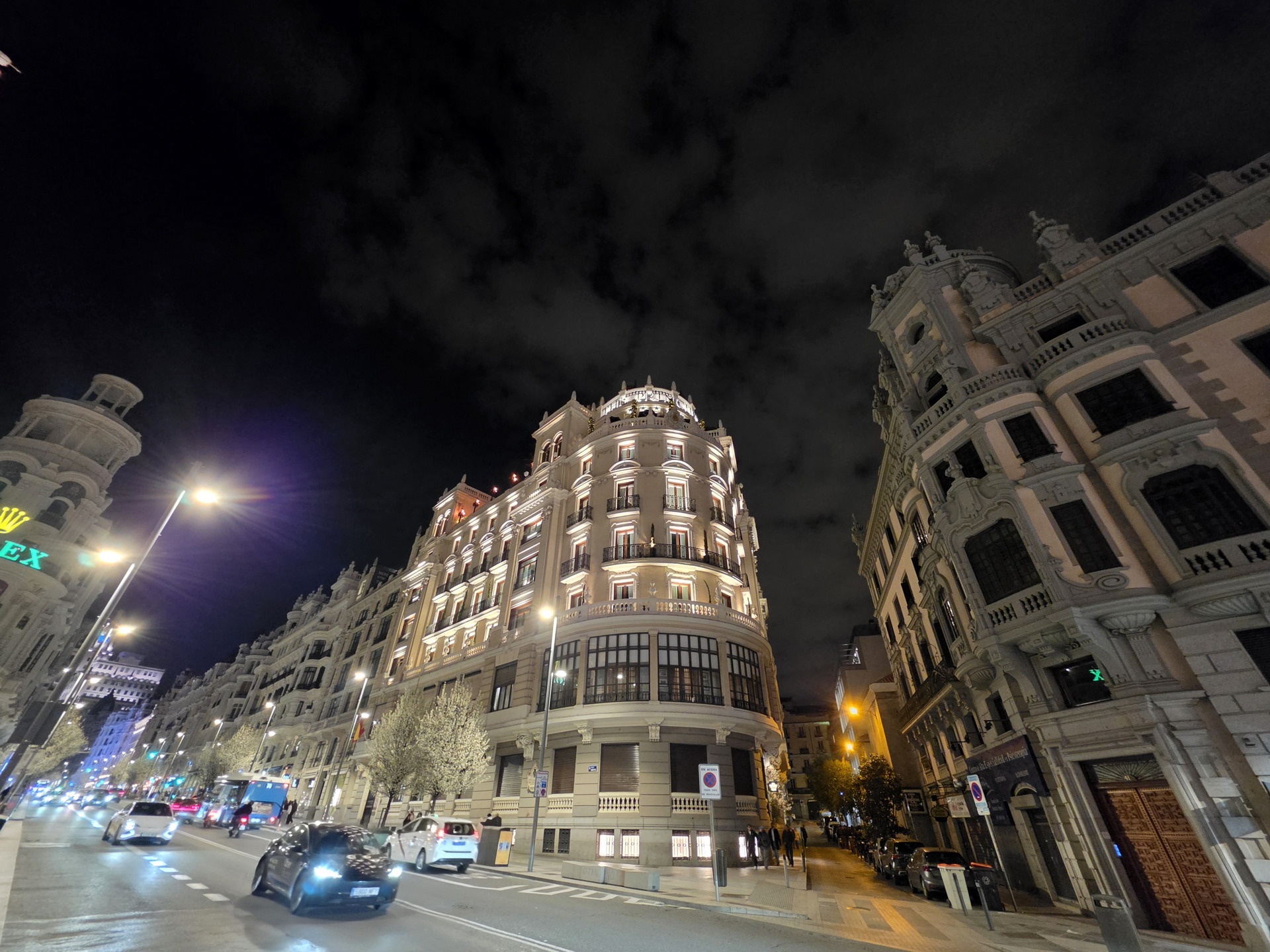 Calles iluminadas de Madrid por la noche, con edificios históricos y coches en movimiento.