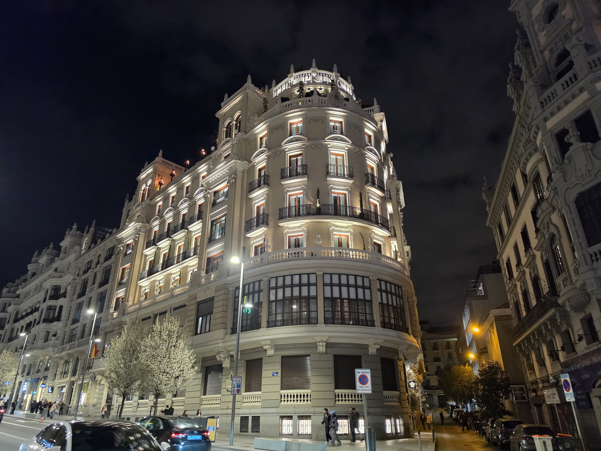 Edificio iluminado en una calle de Madrid por la noche, con cielo oscuro y vehículos circulando.