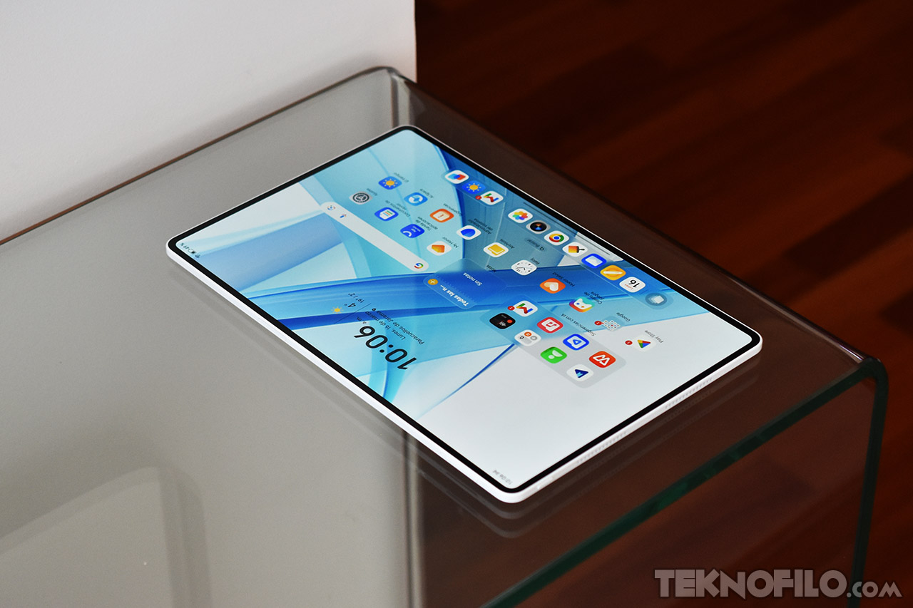 Tablet moderna en mesa de vidrio mostrando aplicaciones y hora a las 10:06. Diseño elegante y funcional.