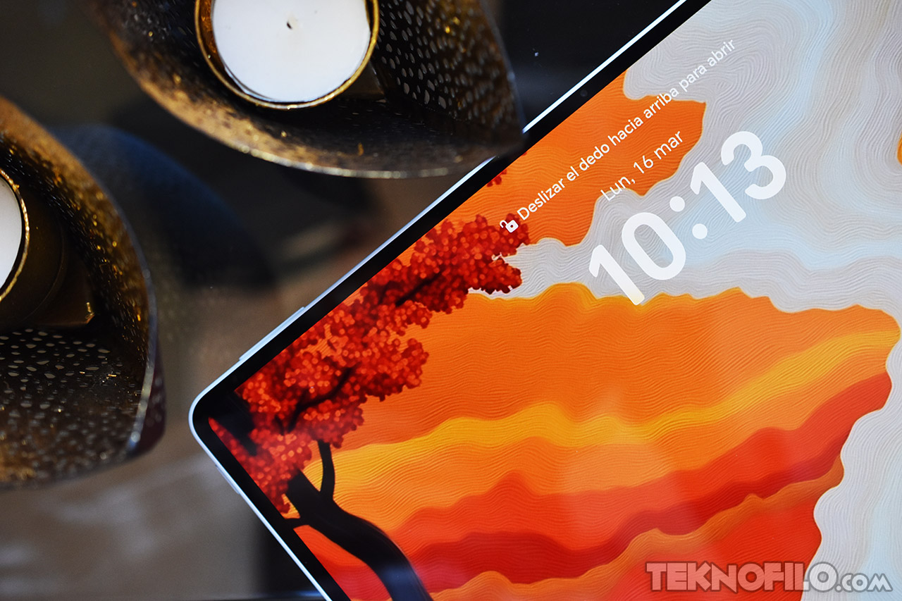 Pantalla de tableta Samsung con fondo colorido y reloj digital a las 10:13 am, cerca de dos velas decorativas.