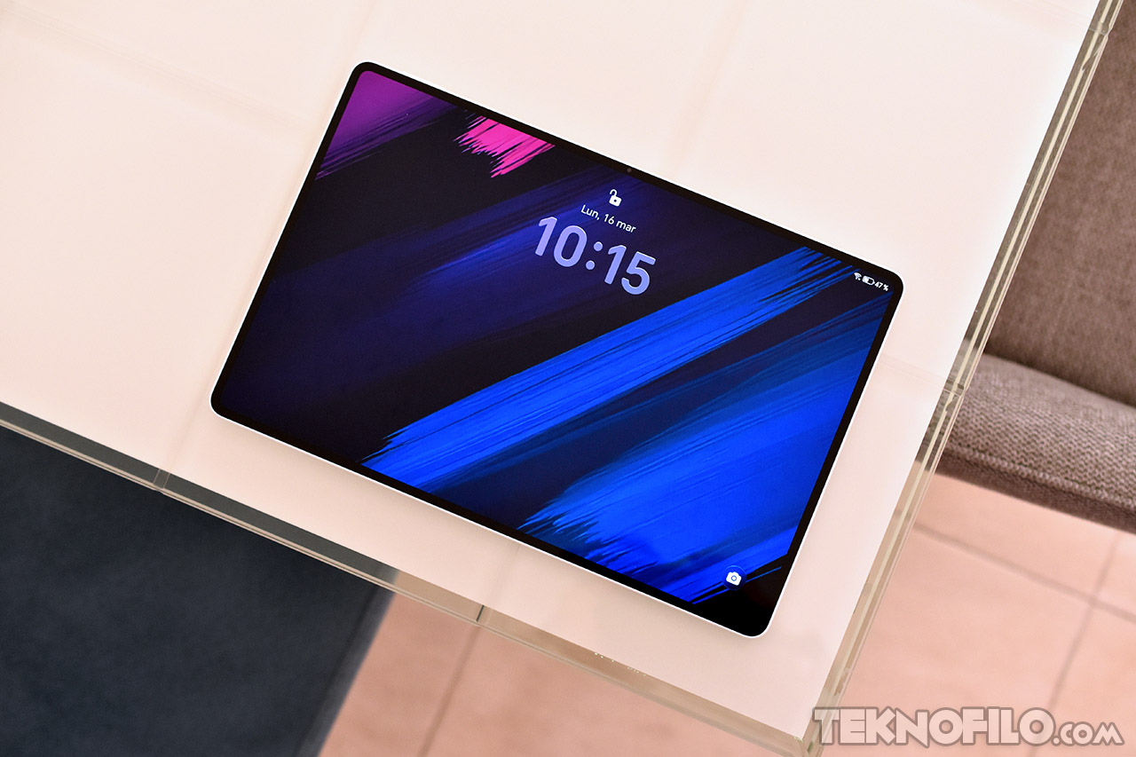 Tablet moderna con pantalla encendida mostrando la hora en diseño minimalista sobre mesa blanca.