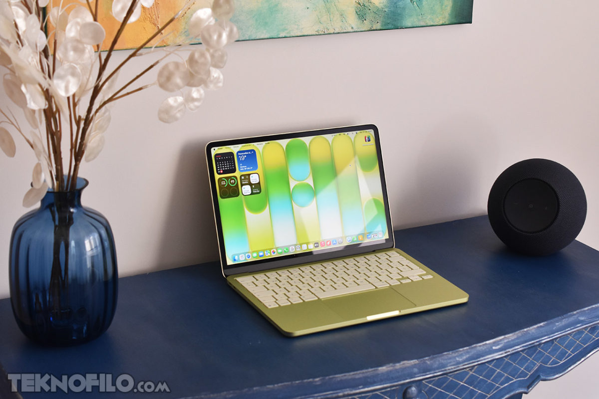 MacBook Neo review en español: Análisis completo, opinión y prueba real Portátil en escritorio azul con altavoz negro y jarrón azul. Pantalla muestra colorido diseño digital.