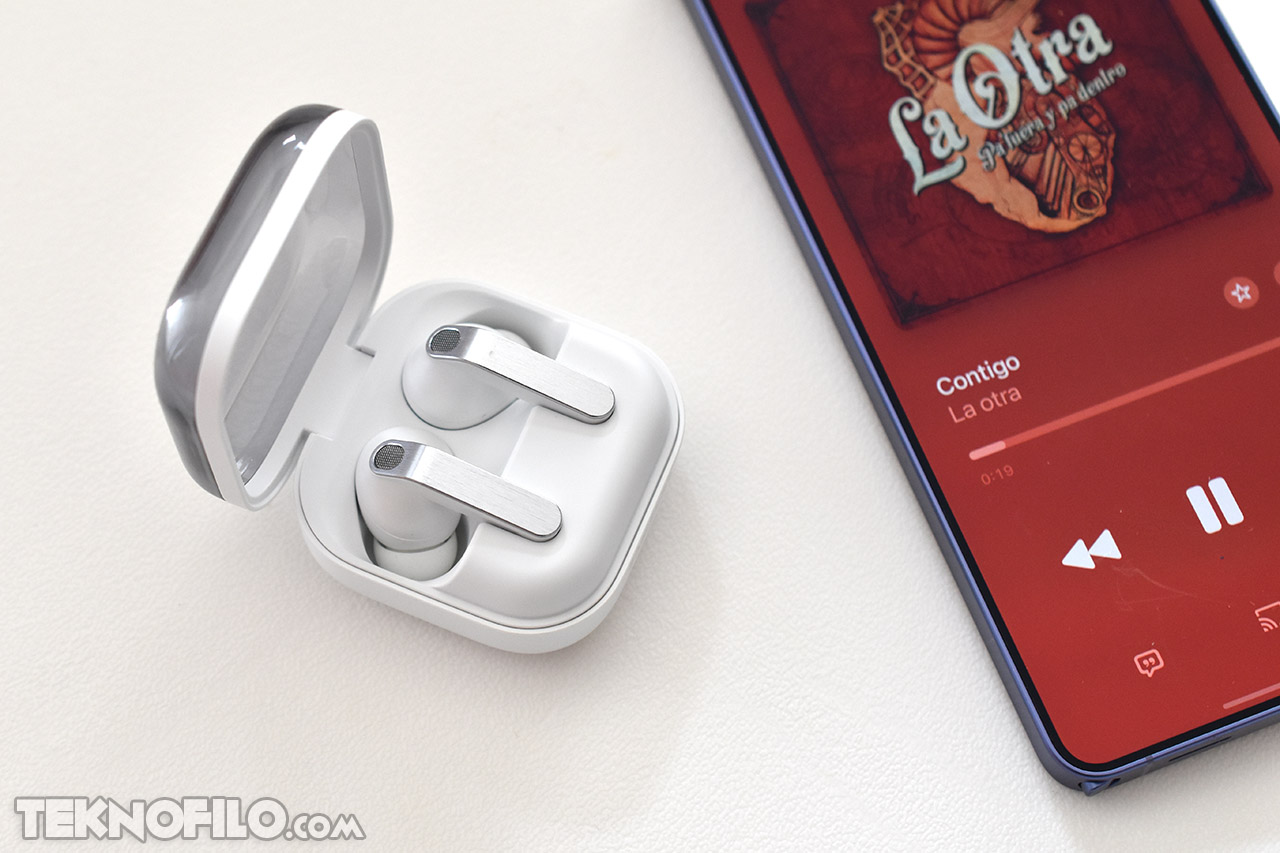 Auriculares inalámbricos blancos junto a smartphone con música en pantalla, color rojo de fondo.