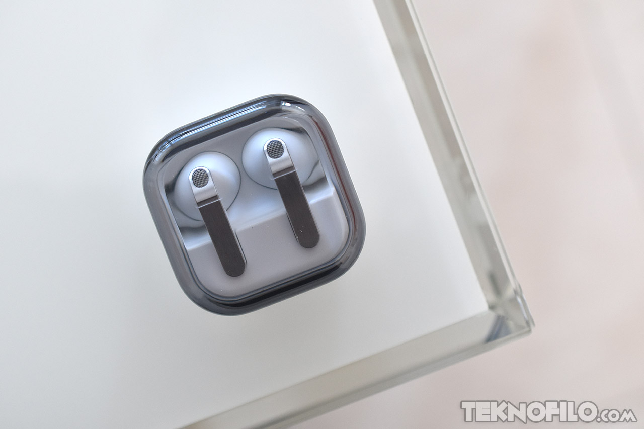 Auriculares inalámbricos en estuche de carga transparente sobre una superficie blanca. Ideal para tecnología portátil.