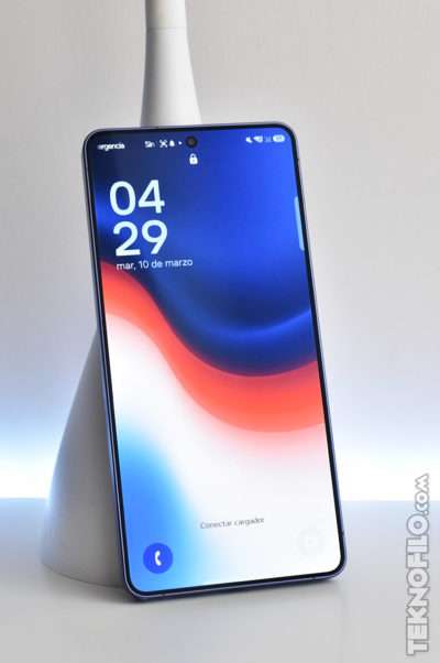 Smartphone moderno con pantalla iluminada mostrando la hora 04:29 y fecha 10 de marzo, ubicado sobre una base blanca.