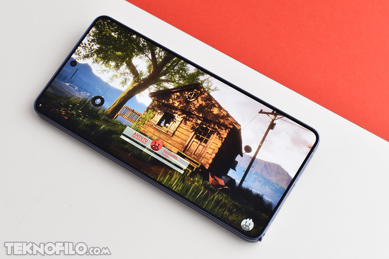 Smartphone mostrando videojuego en pantalla, escena de casa en bosque, prueba de rendimiento AnTuTu.