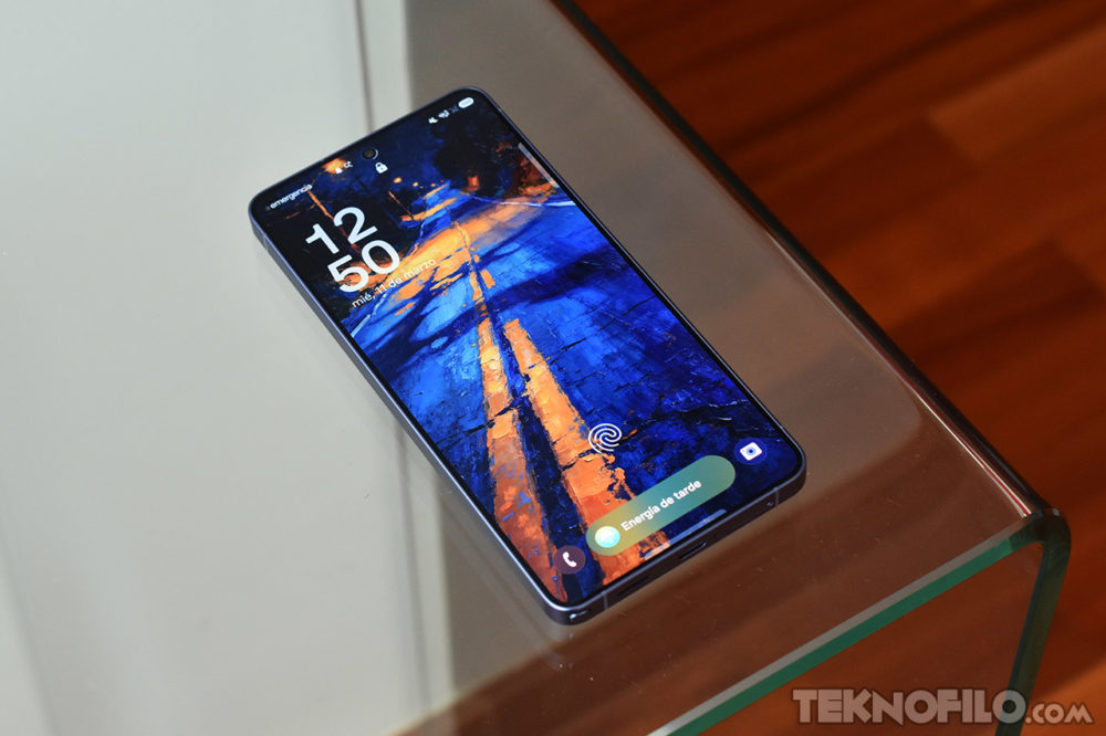 Samsung podría usar pantallas BOE en el Galaxy S27 para reducir costes Smartphone sobre mesa de vidrio con pantalla encendida, mostrando un fondo artístico en tonos azul y naranja.