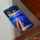 Smartphone sobre mesa de vidrio con pantalla encendida, mostrando un fondo artístico en tonos azul y naranja.