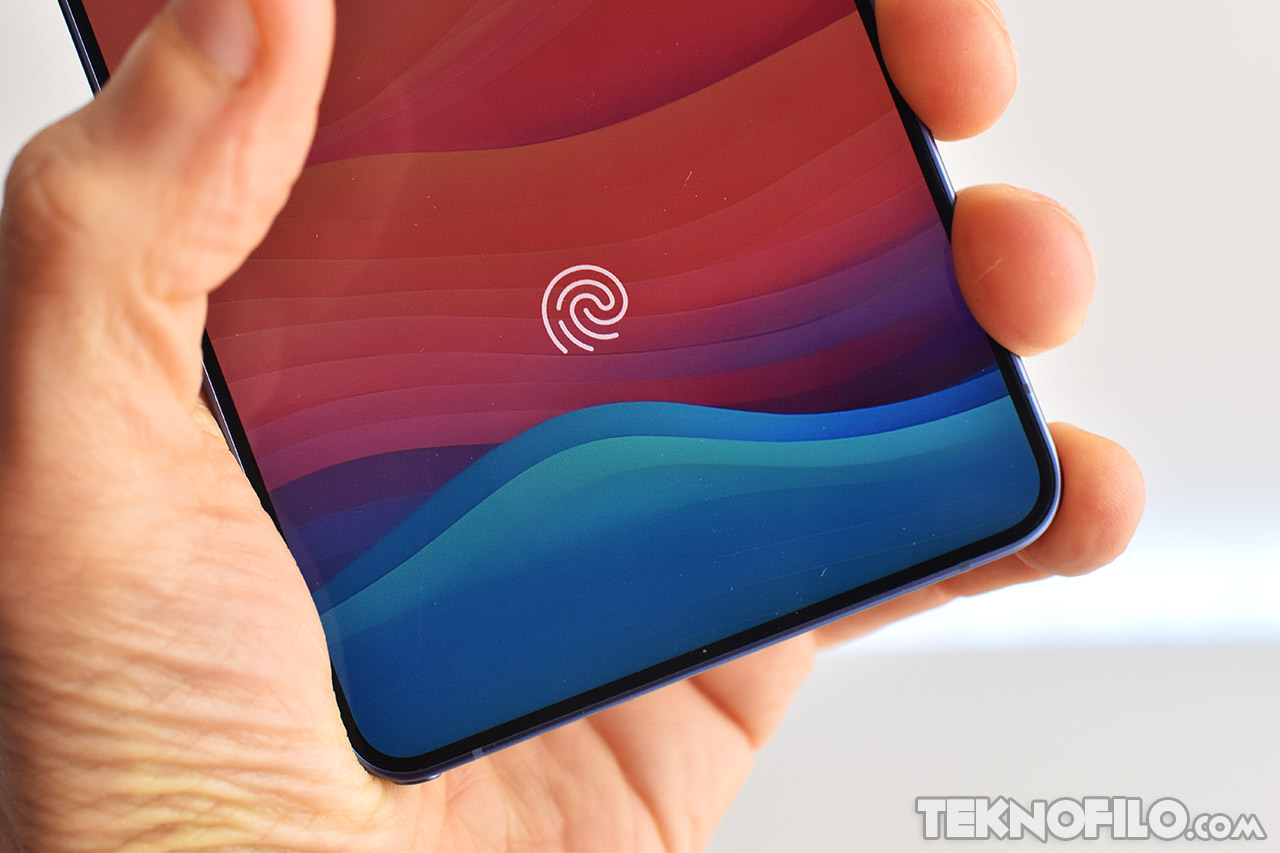 Smartphone con lector de huellas en pantalla sujetado por una mano, fondo de colores ondulados.