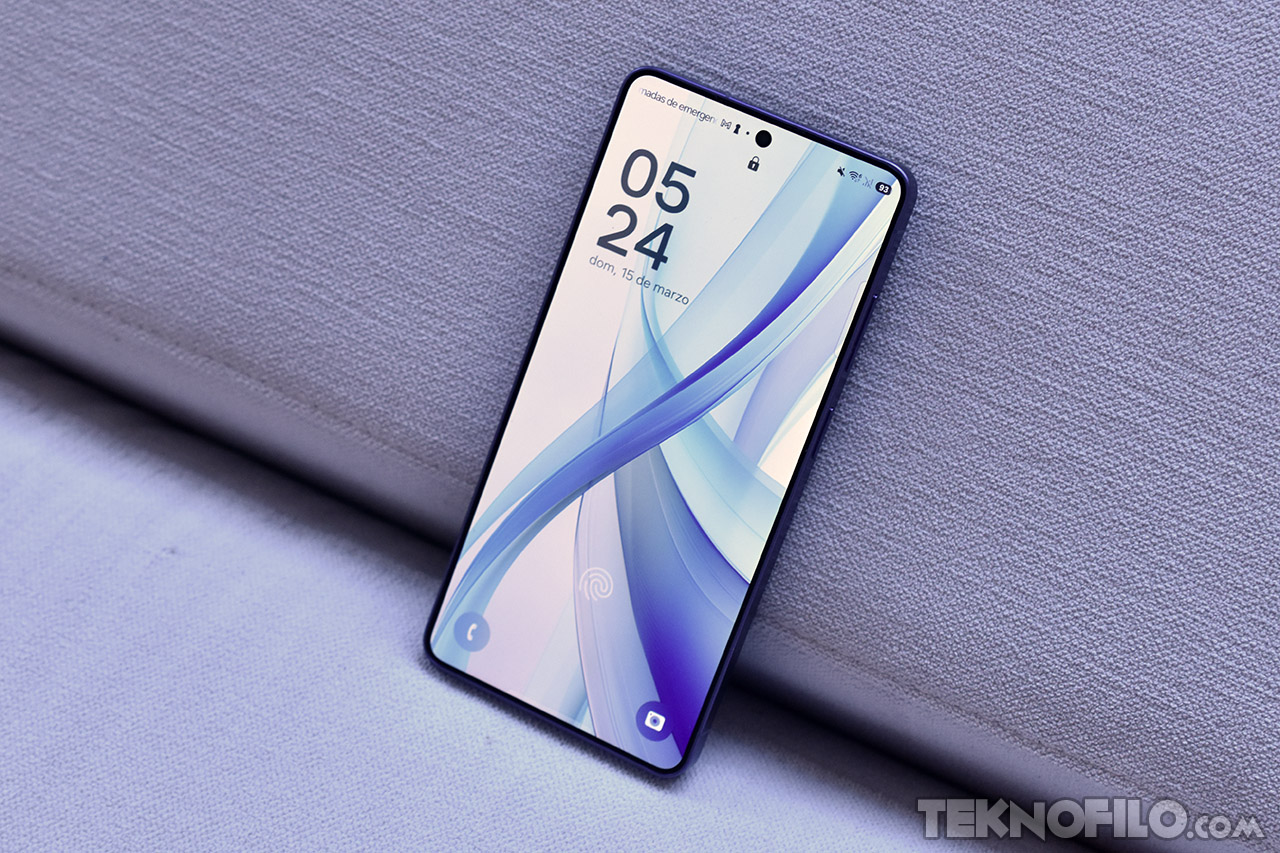 Smartphone moderno sobre sofá mostrando pantalla de inicio con fondo azul y hora en pantalla.