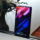 Smartphone con pantalla de inicio colorida sobre base de vidrio, junto a planta decorativa.