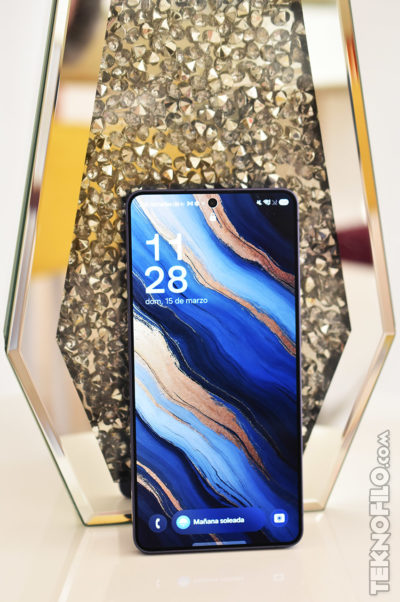 Smartphone con fondo de pantalla azul y dorado frente a una decoración brillante. Hora mostrada: 11:28.