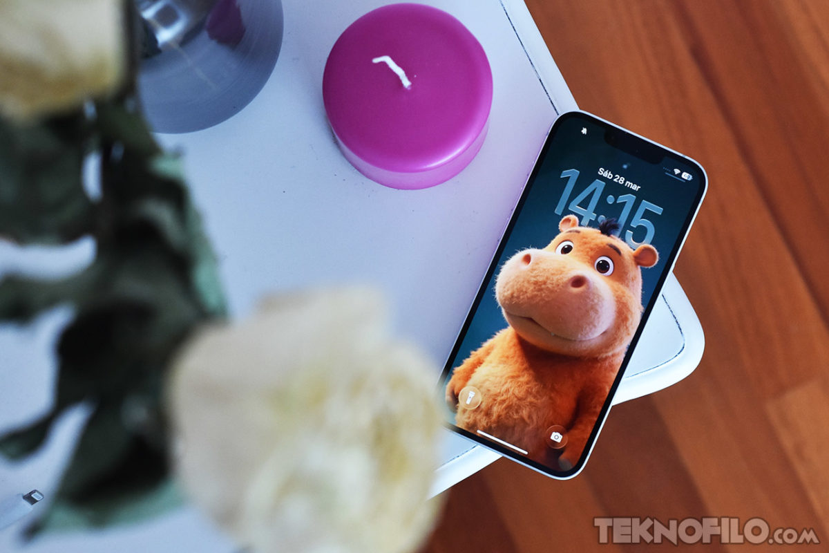 Análisis del iPhone 17e a fondo y opinión Teléfono sobre mesa con fondo de pantalla de personaje animado, junto a una vela rosa y flores desenfocadas en primer plano.