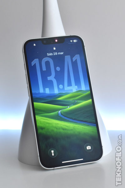 Smartphone moderno con fondo de pantalla de colinas verdes, pantalla encendida mostrando la hora 13:41.