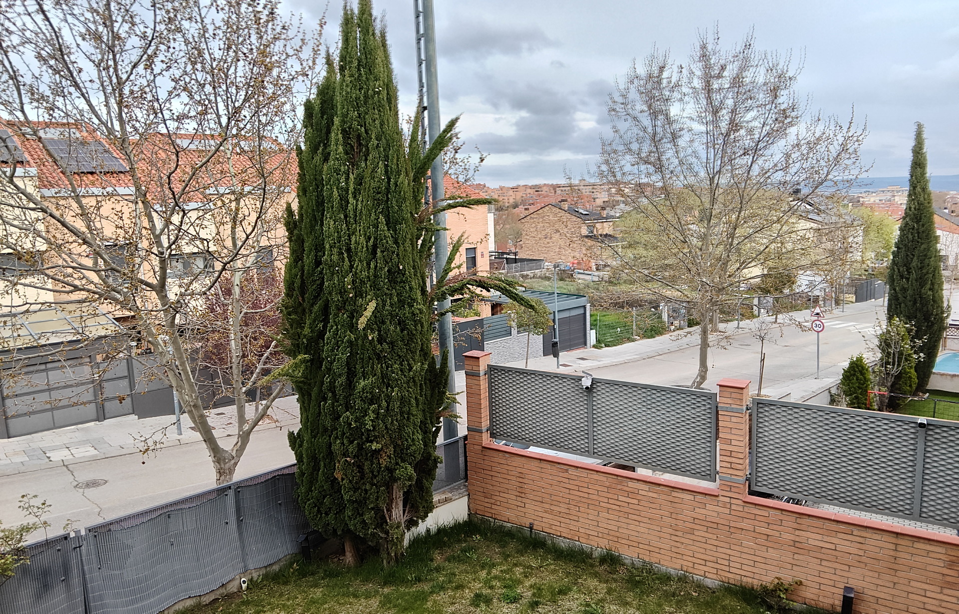 Vista de un barrio residencial con árboles, césped y cielo nublado.