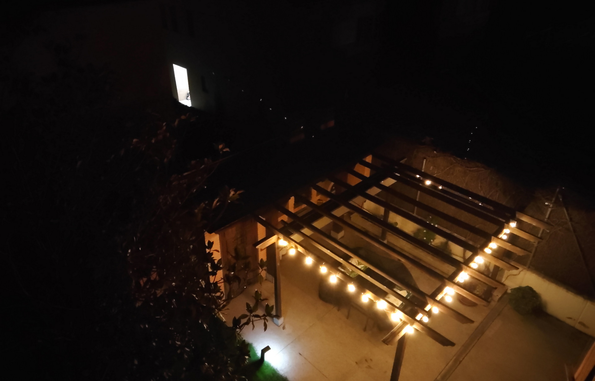 Terraza iluminada con luces cálidas en una noche oscura, vista desde arriba. Ambiente acogedor y relajante.